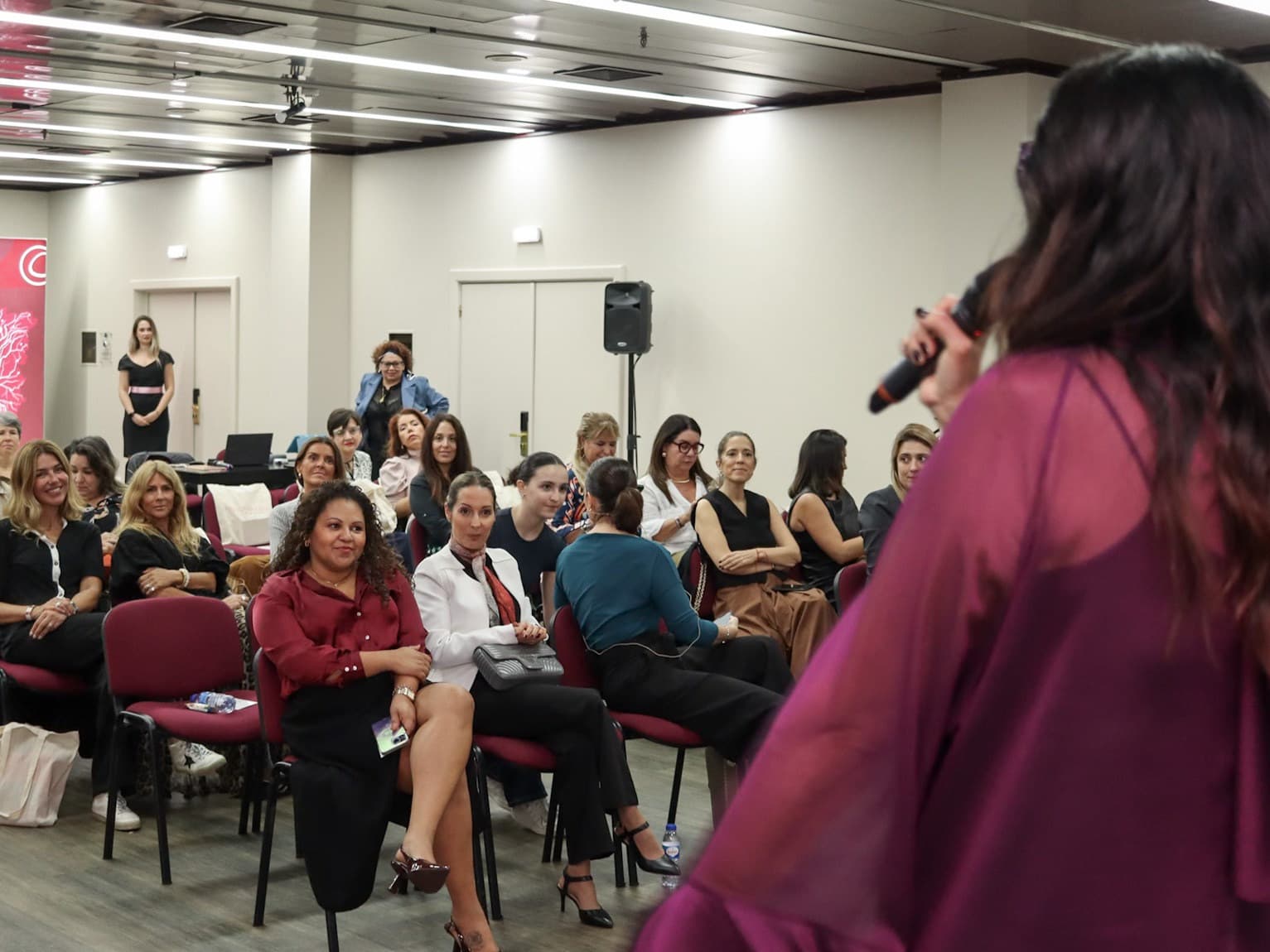 Patrícia Garboni apresentando ao microfone para uma plateia sentada em um evento